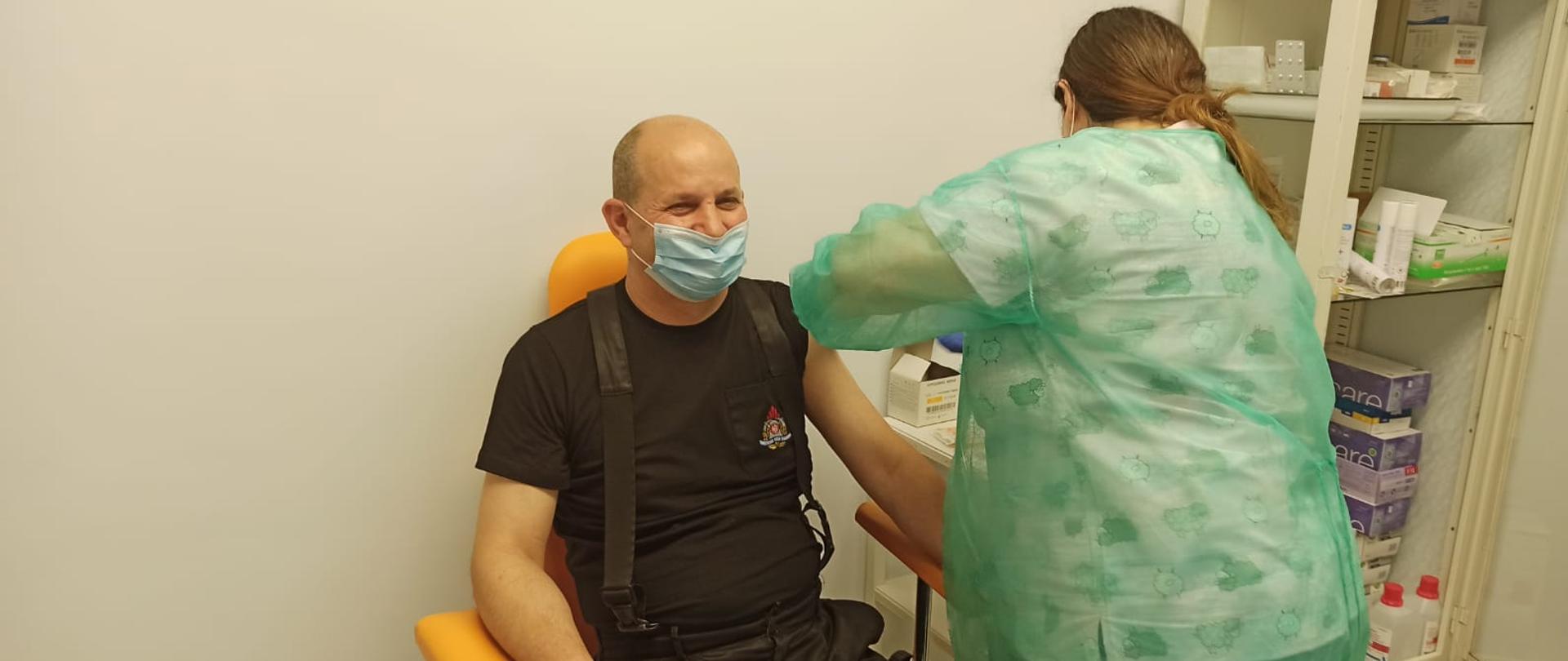 Zdjęcie przedstawia mężczyznę siedzącego na fotelu, który jest sczepiony przez pielęgniarkę.