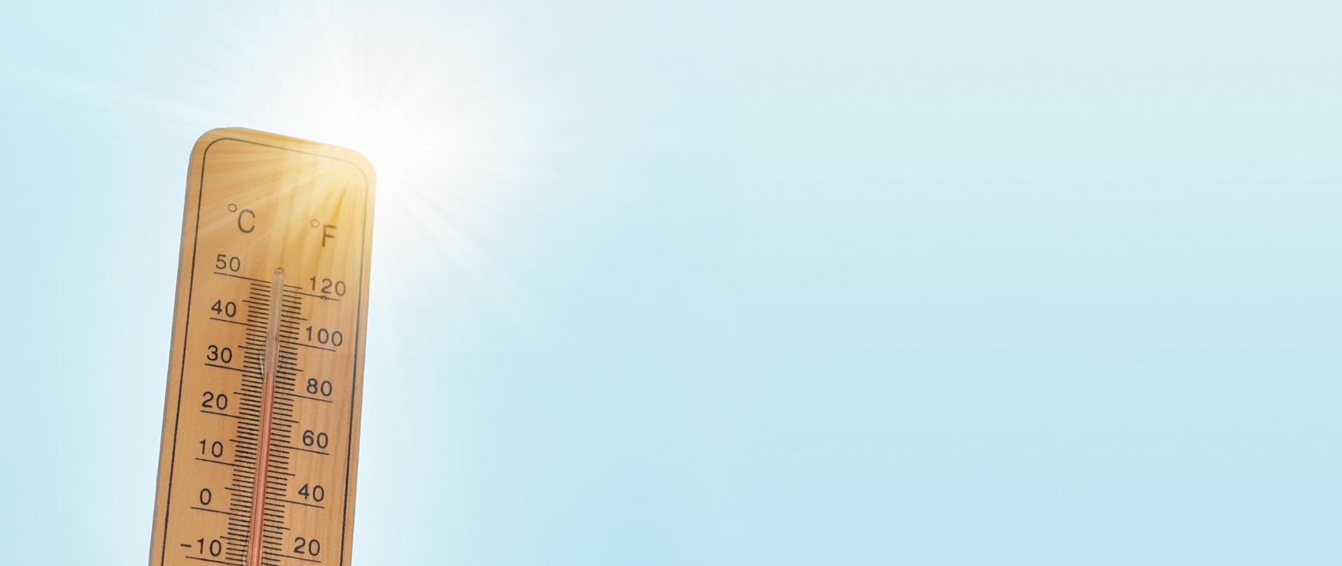 Drewniany termometr na tle jasnoniebieskiego nieba.