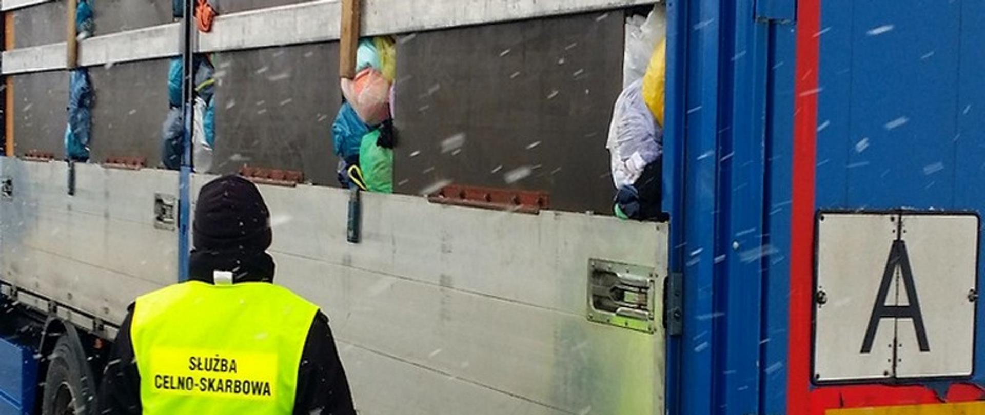 Funkcjonariusz Służby Celno-Skarbowej przy naczepie, przez otwory wystają worki z odzieżą.