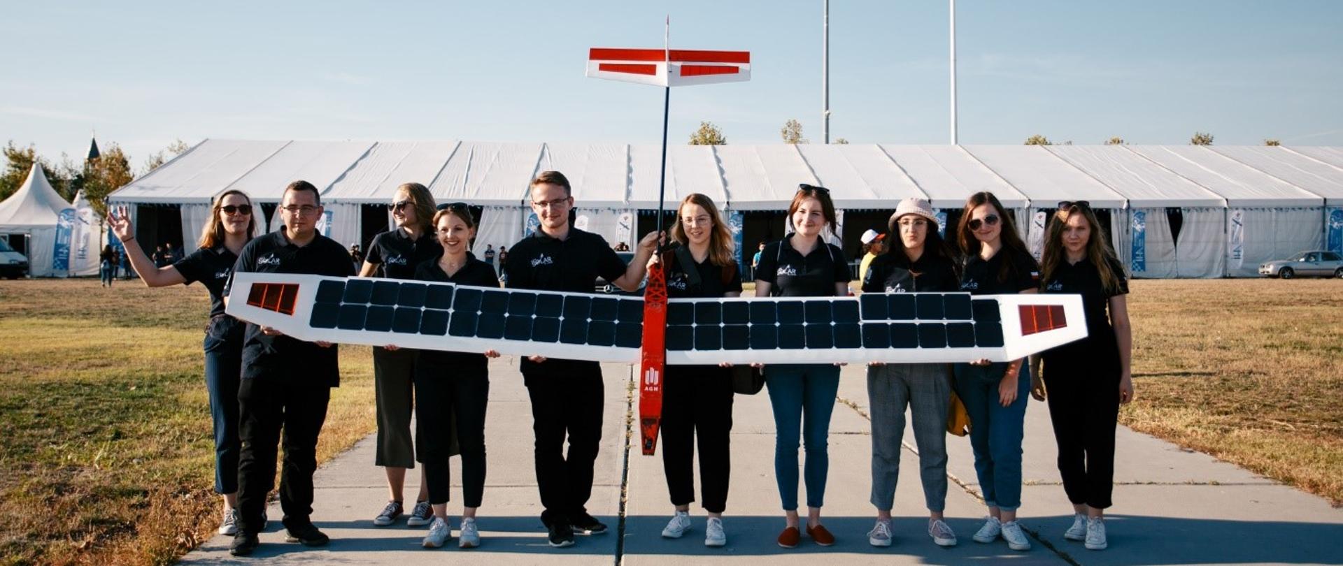 Grupa studentów trzyma samolot, na skrzydłach którego widać rzędy paneli solarnych.