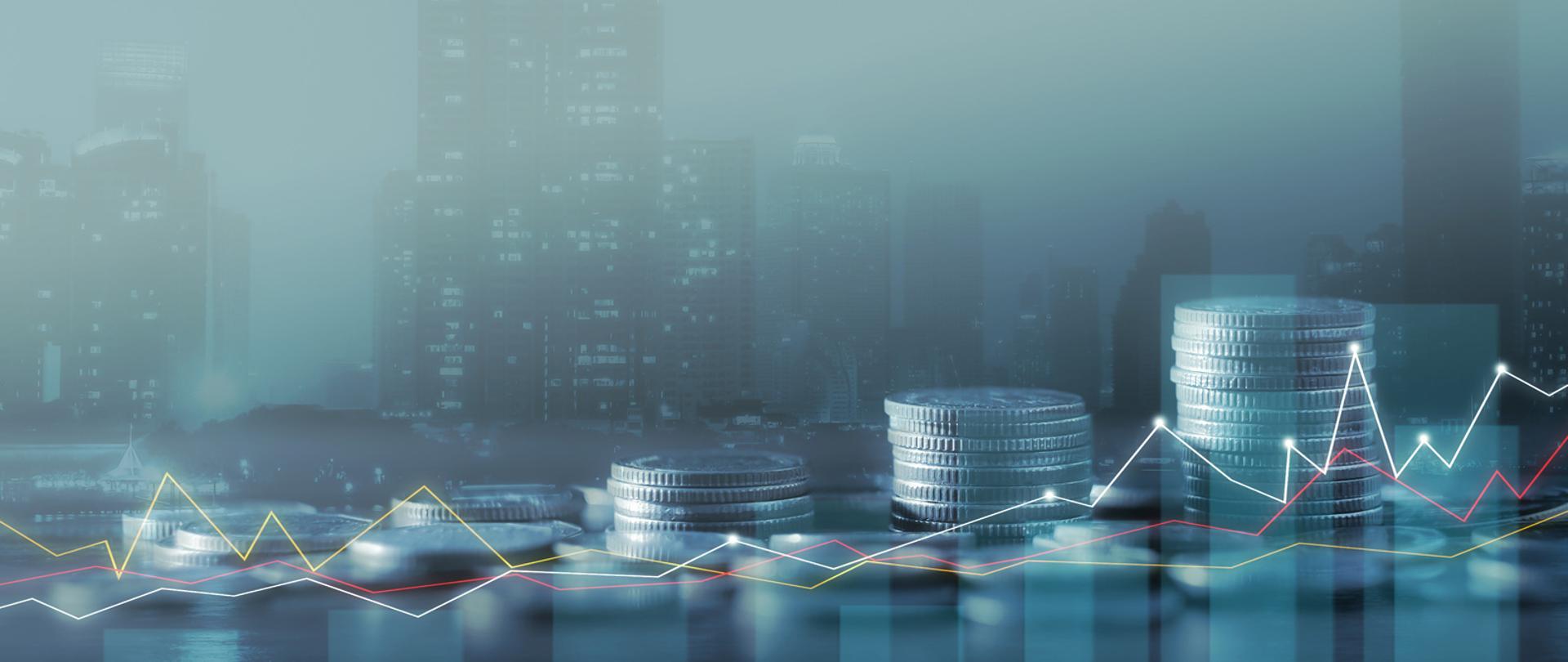 Monety ustawione jedne na drugich, wykresy, w tle panorama miasta.