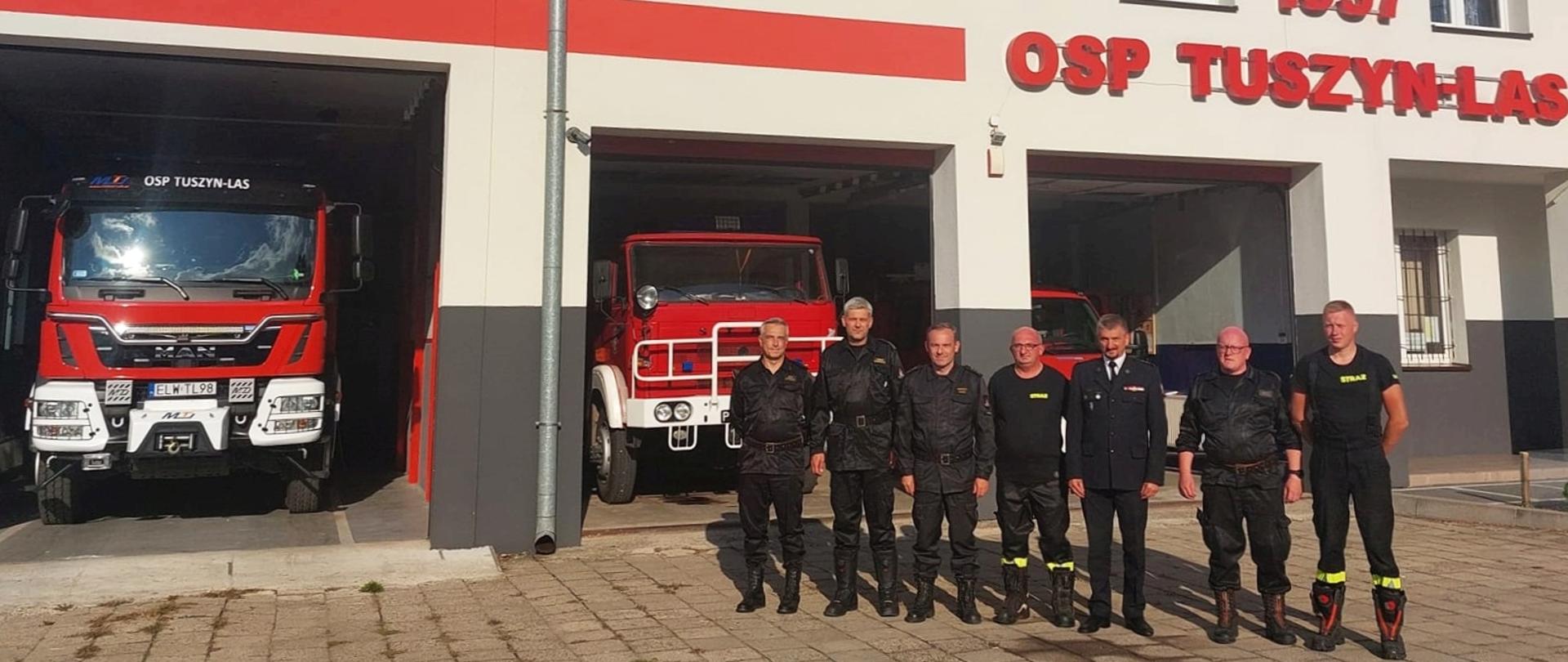 siedmiu strażaków pozujących do zdjęcia przez budynkiem ochotniczej straży pożarnej na budynku napis 1957 OSP Tuszyn - Las