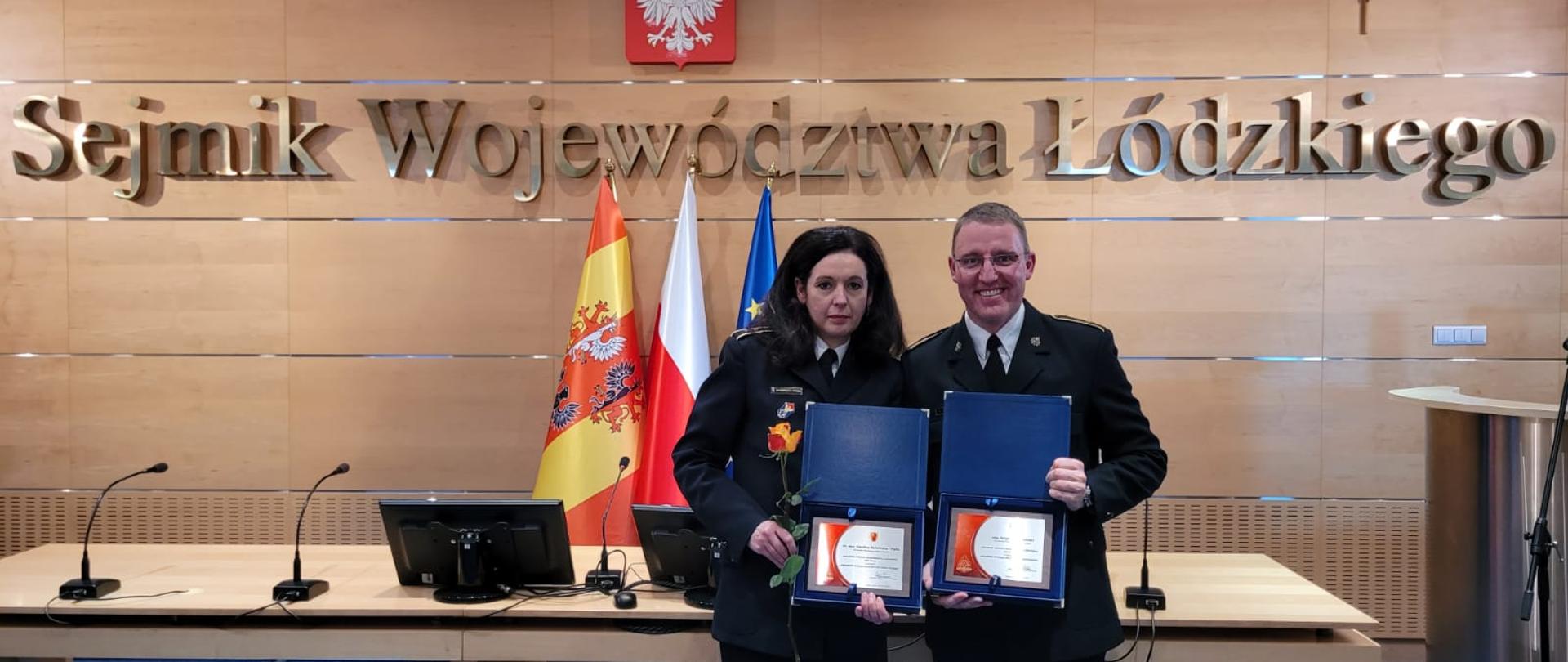 Laureaci KP PSP w Kutnie ubrani w mundury wyjściowe w kolorze granatowym. W ręce trzymają grawertony z gratulacjami. 