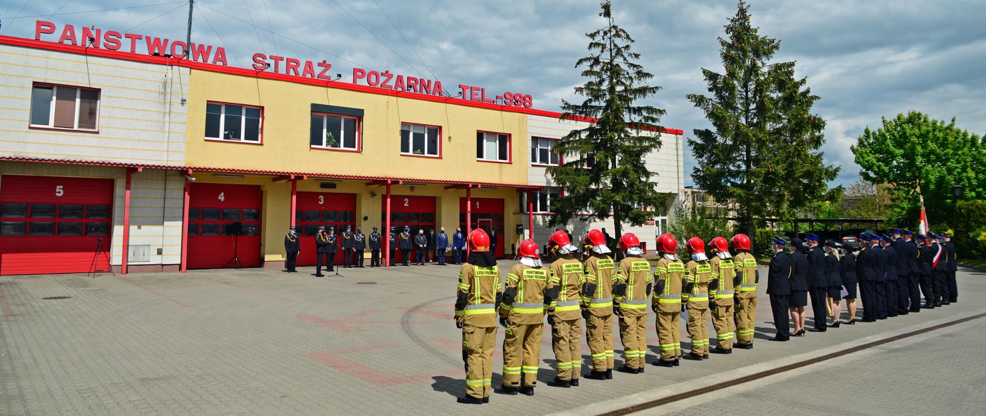 Uroczyste obchody Dnia Strażaka na placu zewnętrznym Komendy Powiatowej. Ujęcie przedstawia wszystkich uczestników uroczystego apelu, zarówno strażaków w szeregu jak i zaproszonych gości na tle budynku Komendy Powiatowej Państwowej Straży Pożarnej w Chojnicach. 
