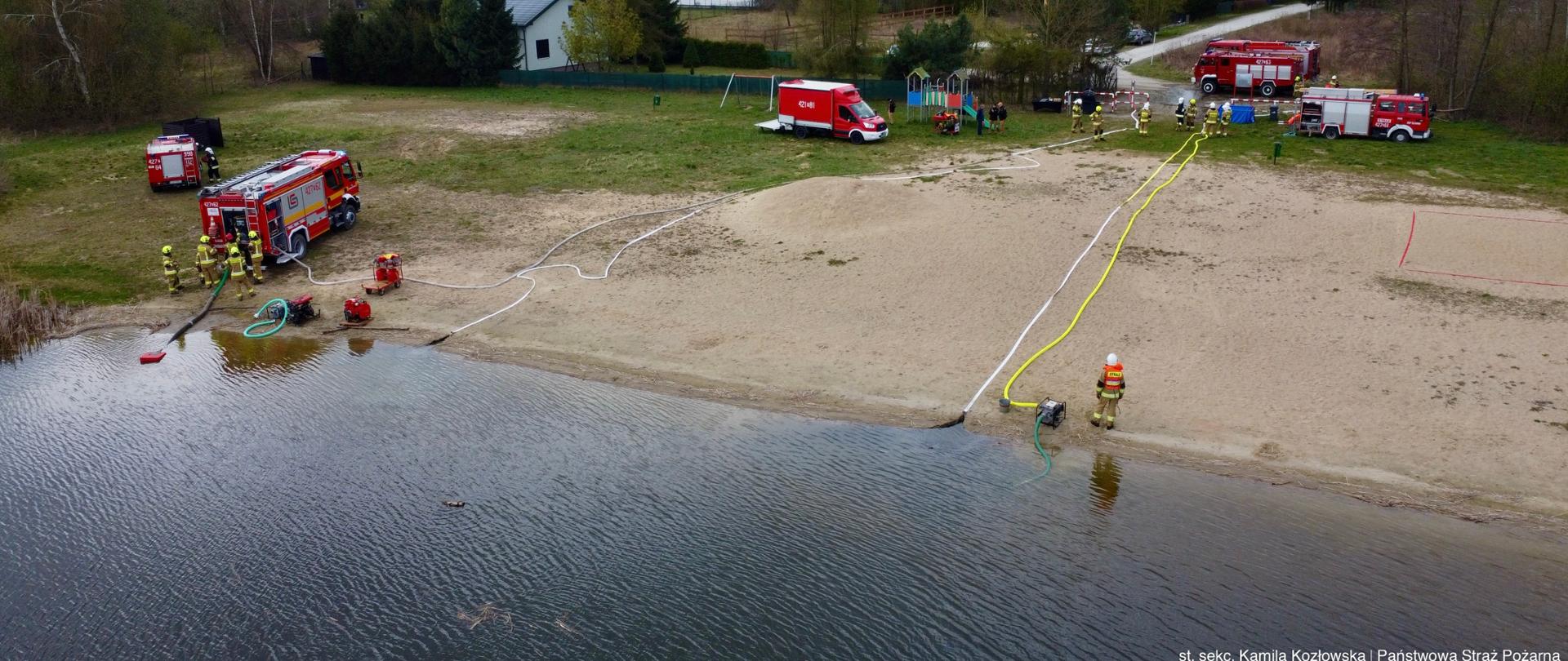Widok na plażę i ćwiczących strażaków oraz ich wozy