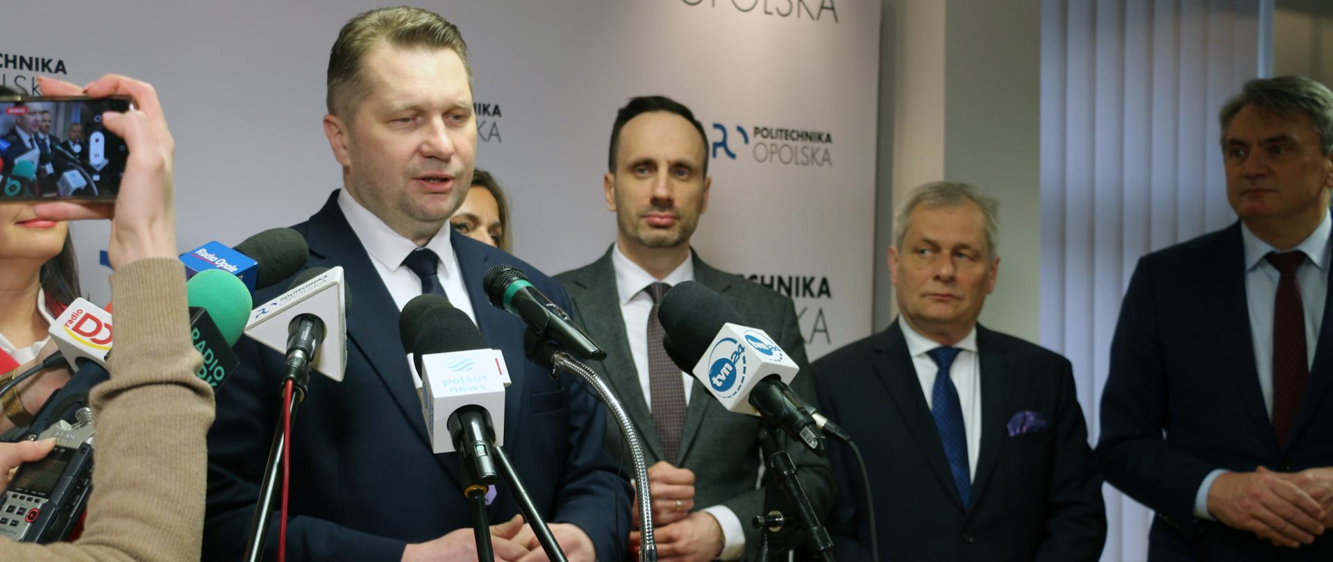 Na zdjęciu minister Czarnek, stojący przed dziennikarzami. Przemawia do ustawionego mikrofonu. W tle pozostali uczestnicy konferencji prasowej - w tym wojewoda opolski. 