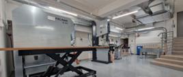 Na zdjęciu widzimy wnętrze hali maszyn po remoncie. W pomieszczeniu ustawione są nowoczesne maszyny służące do obróbki maszyn. Widoczne jest również dodatkowe wyposażenie oraz instalacja wentylacyjna oraz odciągowa trocin i pyłu z drewna