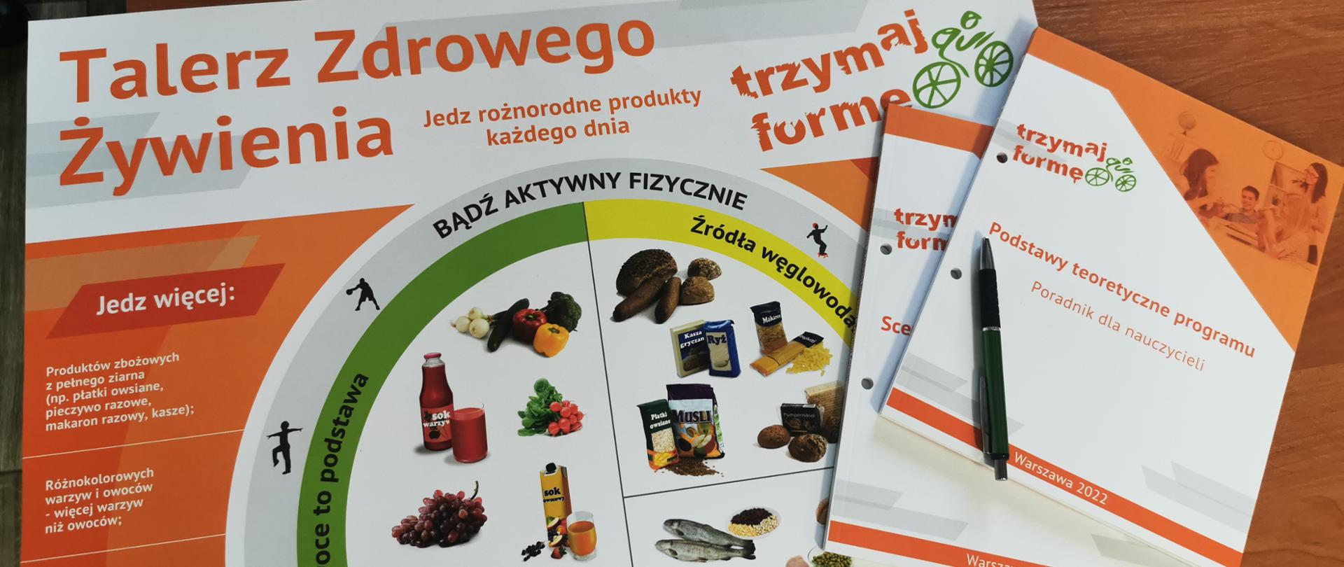 Na stole leży poradnik dla nauczyciela z podstawami teoretycznymi programu, scenariusze opracowane w ramach programu „Trzymaj Formę!”, plakat Talerz Zdrowia oraz długopis z logo programu.
