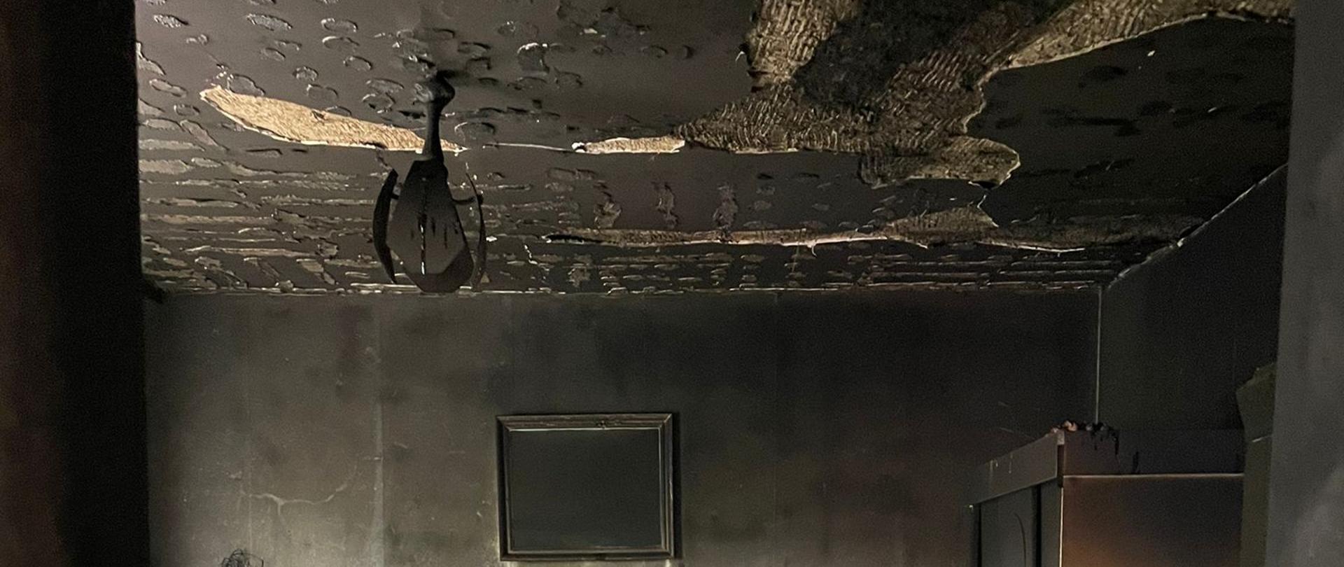 Jedno z pomieszczeń mieszkania w którym powstał pożar. Na suficie spaliły się kasetony, ściany zostały pokryte sadzą, nadpalone meble od góry. 
