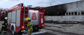 Zdjęcie przedstawia samochód jednostki Ochotniczej Straży Pożarnej Lubomierz oraz dwóch strażaków podczas działań gaśniczych na terenie zakładu. W tle widoczny jest budynek, w którym doszło do pożaru.