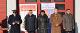 Przemawiający Komendant Powiatowy PSP w Ostrowcu Św., obok zaproszeni goście, na tle Komendy Powiatowej PSP w Ostrowcu Św. 