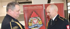 Komendant brygadier Marcin Mazurkiewicz w mundurze wyjściowym ściska dłoń i wręcza dokument odchodzącemu na zaopatrzenie emerytalne