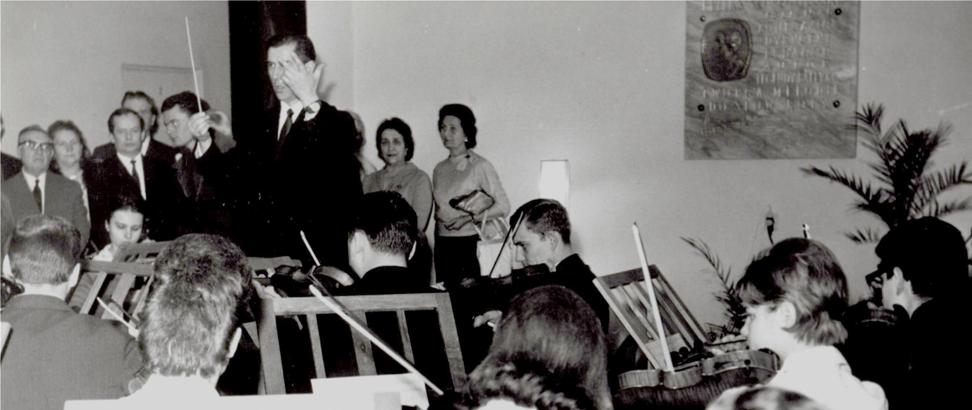 Grafika przedstawia muzykujących uczniów i zaproszonych gości w czasie uroczystości nadania Szkole imienia