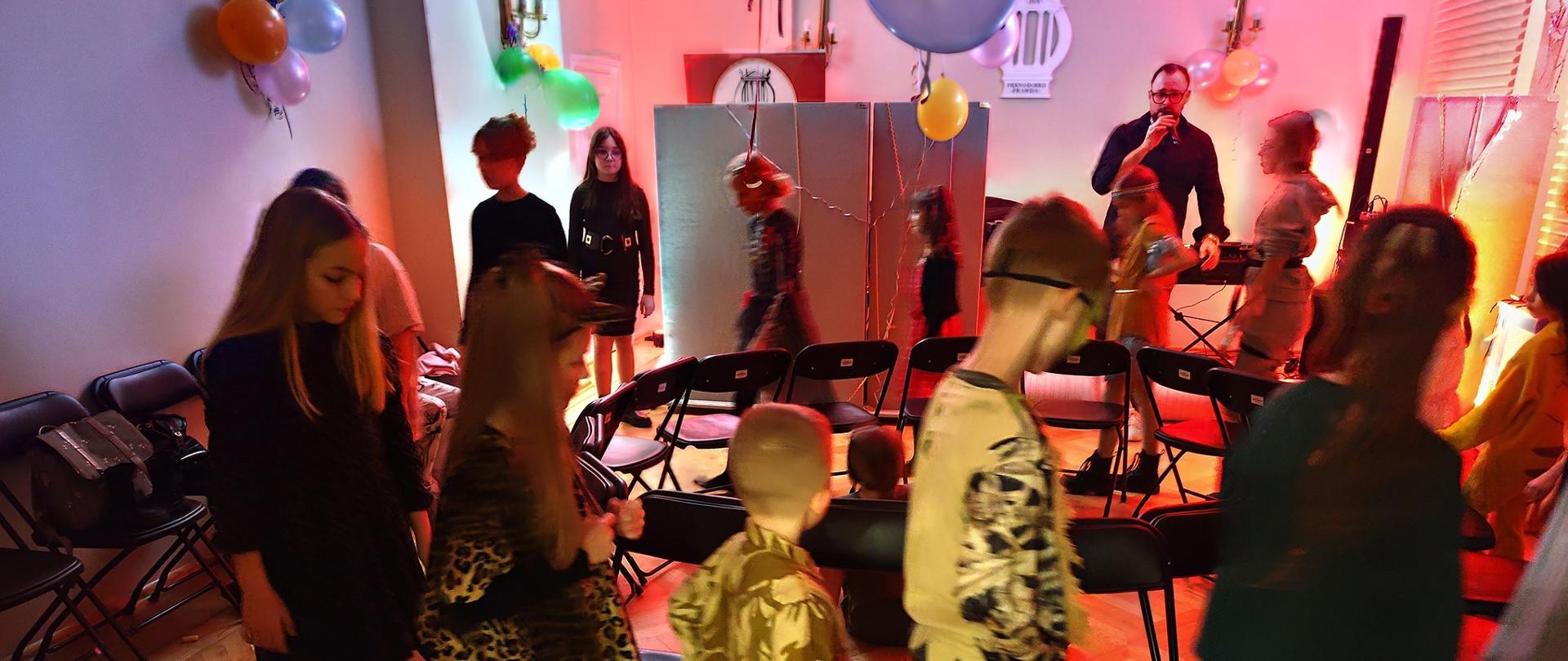 Uczniowie w strojach karnawałowych podczas zabawy, chodzący dookoła krzeseł.