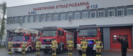 Zdjęcie przedstawia strażaków z KP PSP Opatów oddających honory. W tle stoją 3 samochody pożarnicze oraz budynek Komendy PSP w Opatowie.