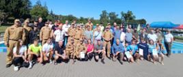 Wspólne pamiątkowe zdjęcie, kończące zawody pływackie na tle basenu. Są obecni przedstawiciele wszystkich służb mundurowych, w tym Leśników, policjantów, strażaków Państwowej Straży Pożarnej i Ochotniczej Straży Pożarnej, młodzieży szkolnej, Wodnego Ochotniczego Pogotowia Ratowniczego oraz Władz samorządowych i zaproszonych gości.