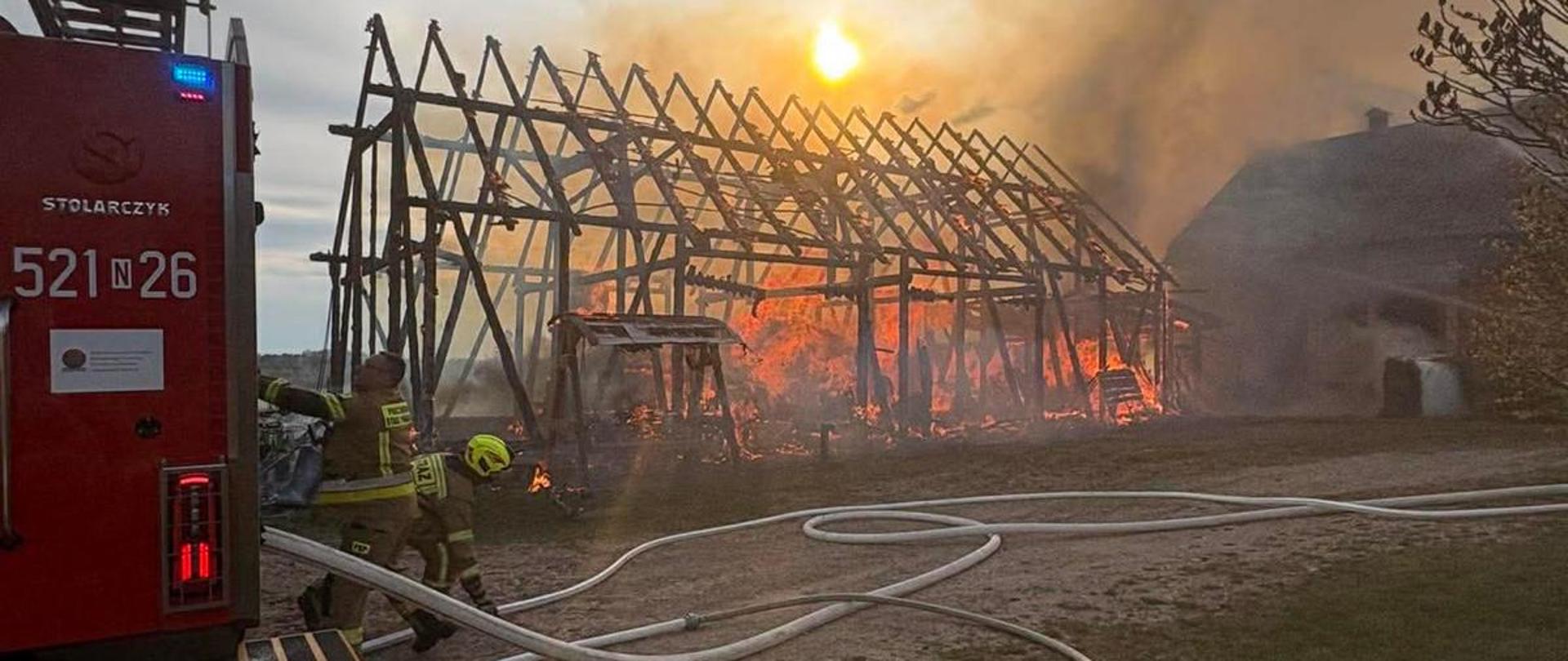 Paląca się stodoła oraz zastęp straży pożarnej podczas rozwinięcia bojowego.