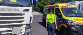 Funkcjonariuszka przy ambulansie i ciężarówce