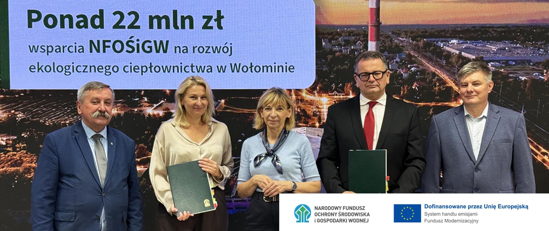 Zdjęcie grupowe z podpisania umowy o dofinansowanie budowy 18 pomp ciepła na terenie ciepłowni w Wołominie. Na zdjęciu od lewej strony: Józef Matysiak, Zastępca Prezesa Zarządu Narodowego Funduszu Ochrony Środowiska i Gospodarki Wodnej, Łucja Sromecka, Dyrektor Departamentu Ciepłownictwa NFOŚiGW, Elżbieta Radwan, Burmistrz Wołomina, Karol Ciepielewski, Prezes Zarządu ZEC Wołomin, Marek Matys, NFOŚiGW. W prawym dolnym rogu logotyp NFOSiGW oraz Funduszu Modernizacyjnego.