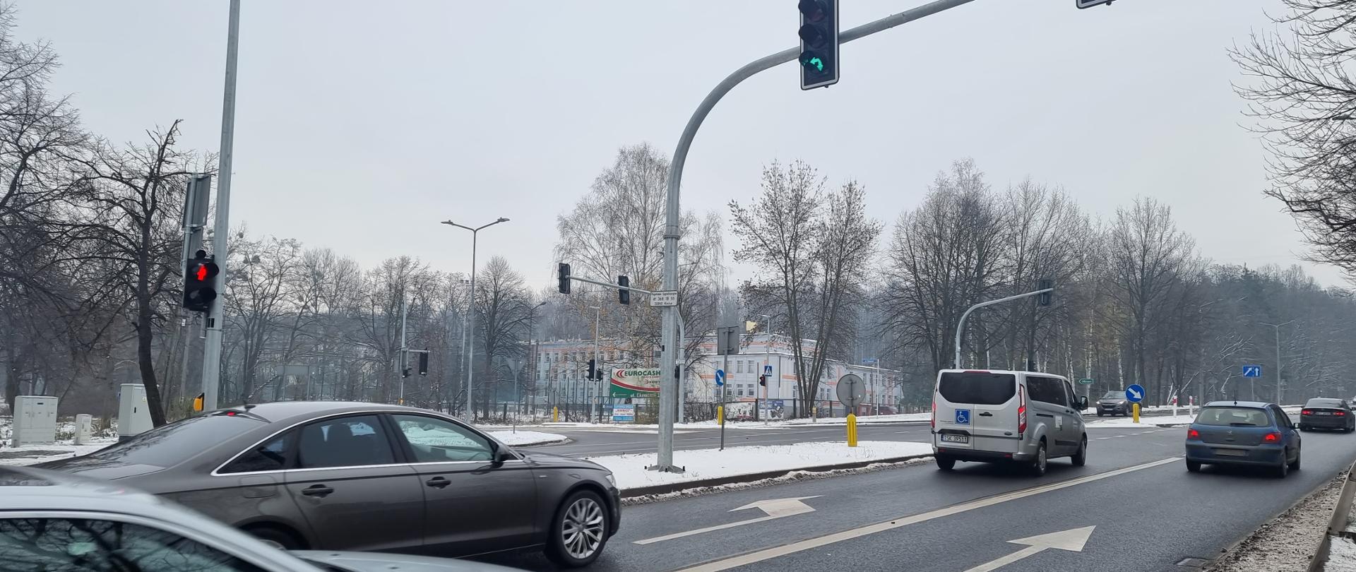 DK42 Skarżysko-Kamienna - skrzyżowanie z sygnalizacją świetlną, dwujezdniowa droga, jadące samochody, sygnalizatory z zielonymi strzałkami, w oddali wjazd z ulicy podporządkowanej 