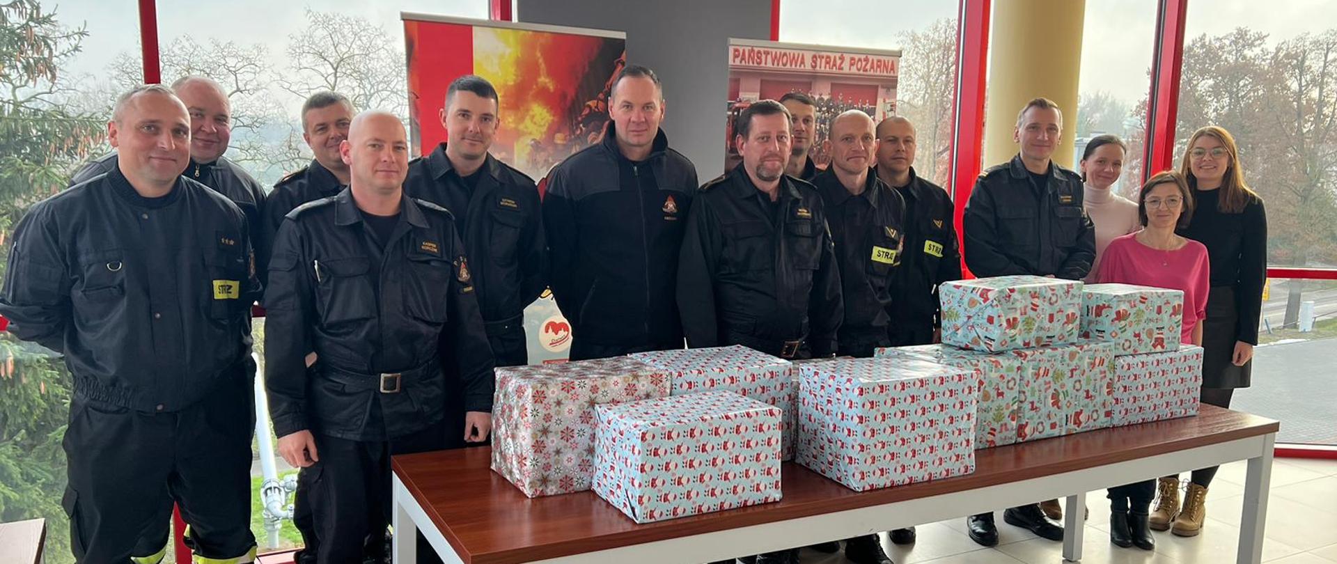 Na zdjęciu znajdują się funkcjonariusze i pracownicy cywilni KP PSP w Chełmnie, na tle prezentów z ramach akcji Szlachetna Paczka. Zdjęcie wykonano w sali sztabowej komendy. 