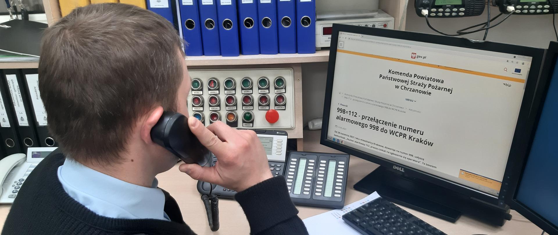 Na zdjęciu dyżurny straży trzyma słuchawkę, wykonuje połączenie testowe do CPR Kraków.