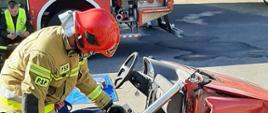Zdjęcie przedstawia użycie przez strażaka rozpieracza kolumnowego w sytuacji wypadku komunikacyjego