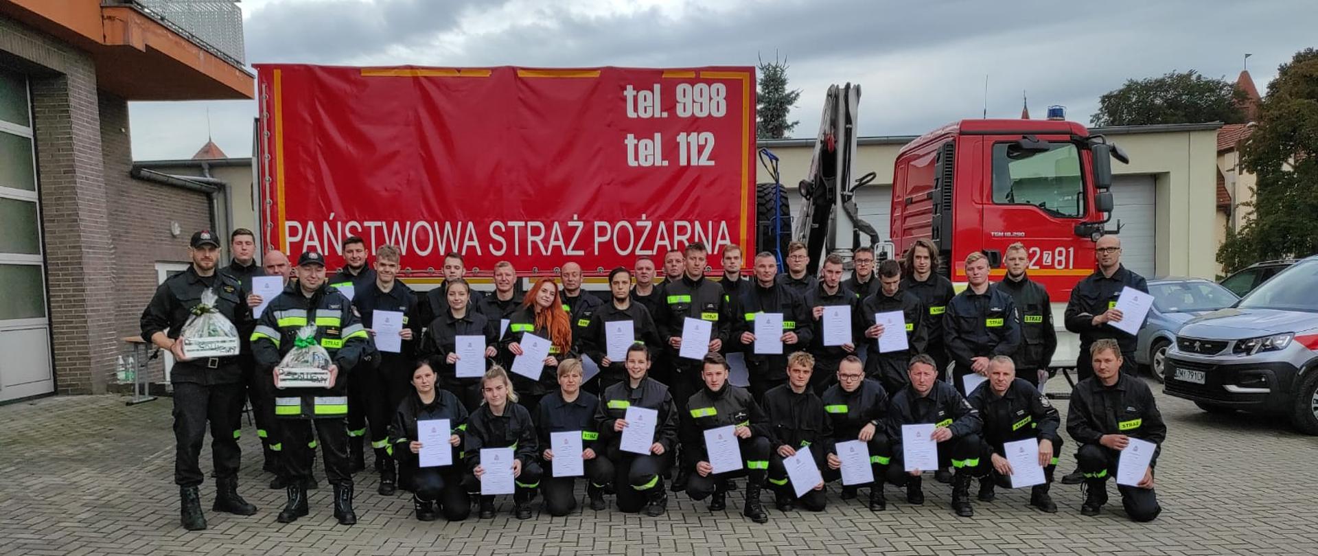 Na zdjęciu widać grupę strażaków w umundurowaniu służbowym. W rekach trzymają zaświadczenia ukończenia szkolenia.