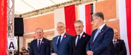 Na zdjęciu trybuna honorowa podczas uroczystości na Placu Zamkowym. Od lewej stroją - wiceminister Czesław Mroczek, minister Tomasz Siemoniak, minister Krzysztof Gawkowski, wicemarszałek Senatu Maciej Żywno. W tle widać innych gości oraz front Zamku Królewskiego z wiszącymi biało-czerwonymi barwami narodowymi. Po lewej stronie kartka "Trybuna A".