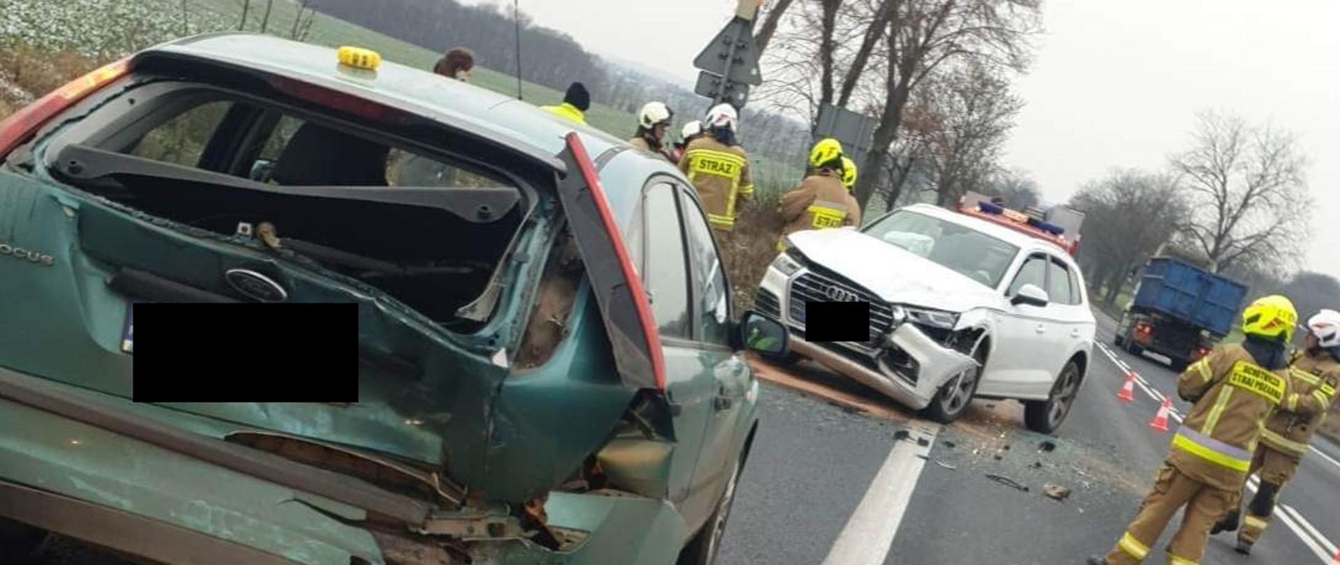 Widać dwa uszkodzone samochody, jeden od tyłu, drugi z przodu, w pobliżu strażacy