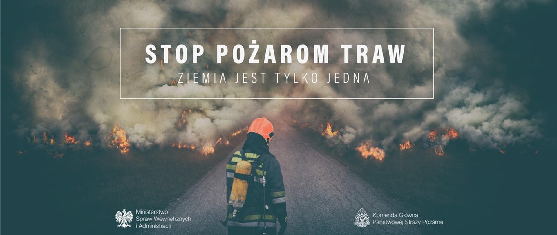 Zdjęcie przedstawia strażaka w ubraniu specjalnym dookoła niego paląca się trawa, bardzo dużo siwego dymu. Strażak stoi pośrodku na asfaltowej drodze odwrócony plecami. W centrum zdjęcia duży napis stop pożarom traw, ziemia jest tylko jedna