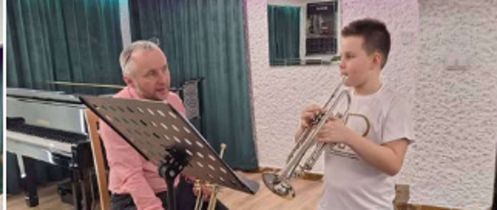 Nauczyciel Tomasz Onysek i uczniowie na tle fortepianu i podświetlonego logo szkoły w sali kameralnej w Państwowej Szkole Muzycznej I stopnia w Lublińcu podczas konsultacji metodycznych w klasie trąbki i eufonium, które prowadził nauczyciel PSM I i II st. w Opolu pan Klaudiusz Lisoń