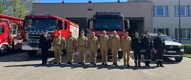 Strażacy z JRG wraz z Komendantami pozują do zdjęcia na tle pojazdów strażackich.
