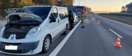 Na zdjęciu widać uszkodzony samochód typu bus marki Renault. Za pojazdem, na pasie awaryjnym zaparkowane dodatkowo pojazdy policji oraz straży pożarnej. Na jezdni widać pomarańczowe pachołki ostrzegawcze oddzielające dwa pasy ruchu.