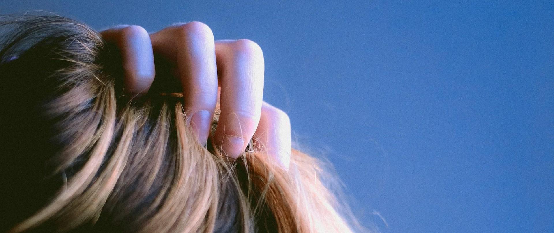 Zdjęcie fragmentu głowy kobiety z długimi włosami z palcami we włosach.