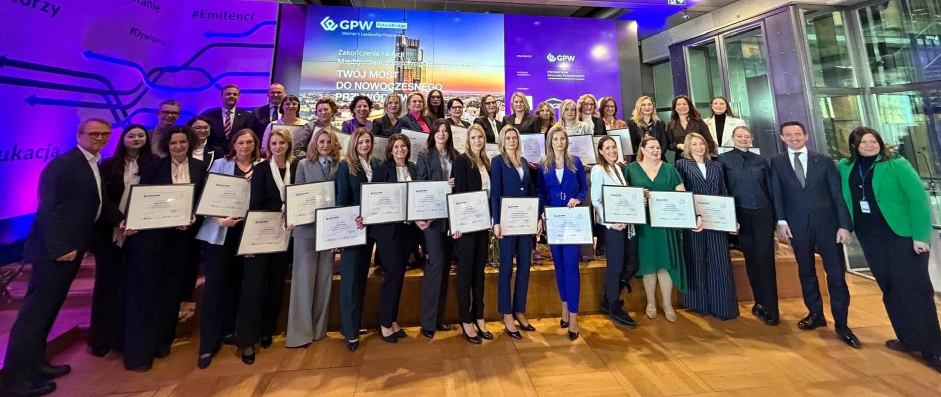 Podsumowanie I edycji Międzyuczelnianego Programu Edukacyjnego GPW Future Bridge - szerokie ujęcie uczestniczek programu wraz z pamiątkowymi dyplomami 