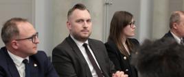 Na zdjęciu wiceminister Konrad Wojnarowski siedzi przy stole konferencyjnym w towarzystwie innych uczestników