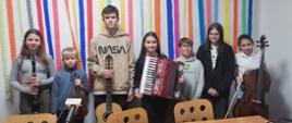 Zdjęcie przedstawia grupę uczniów, pozujących z instrumentami na tle kolorowej ściany.