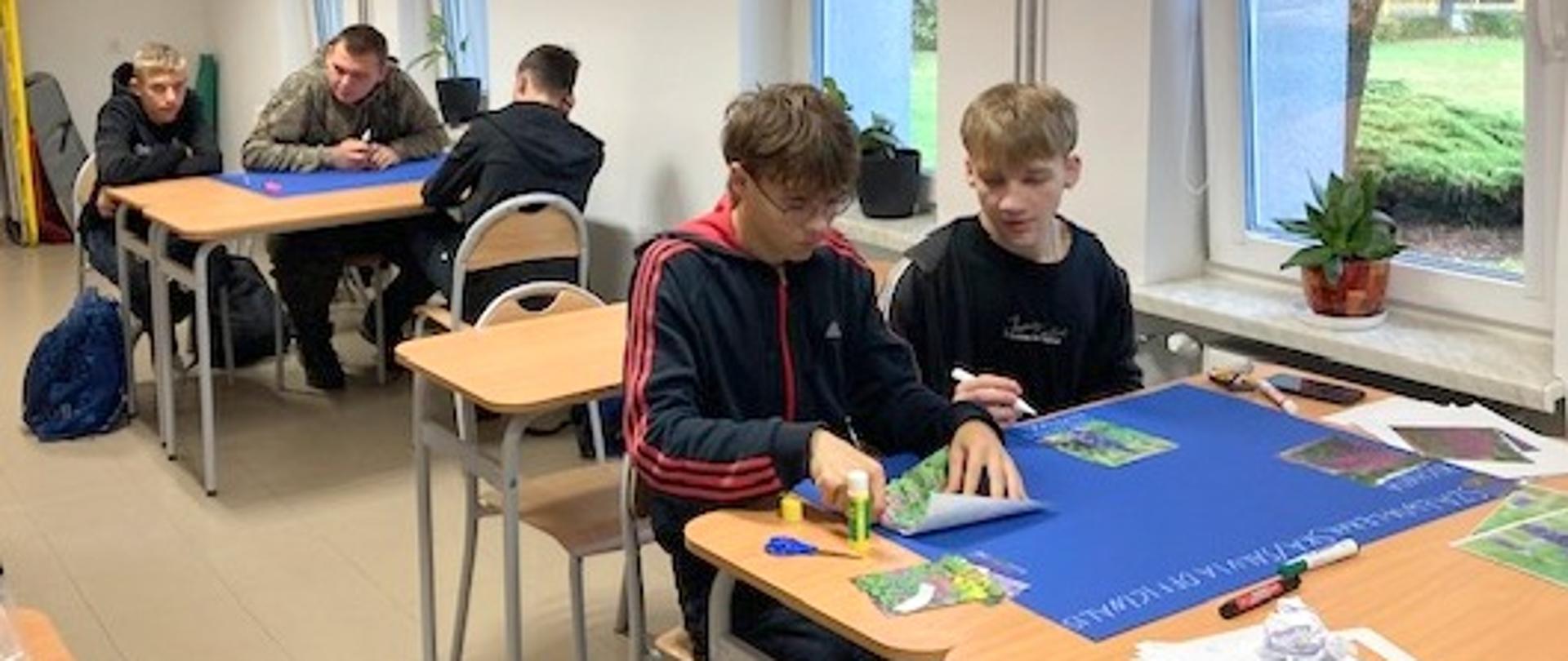 Uczniowie pracują w grupach przy stolikach, przygotowując plakaty.