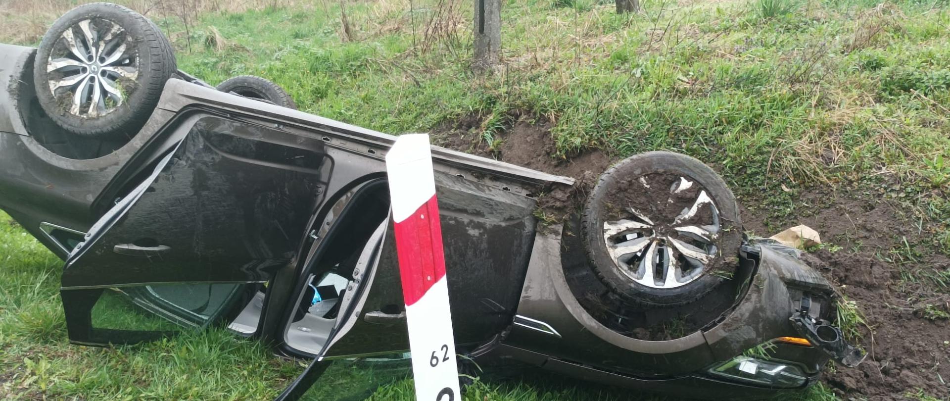 Zdjęcie przedstawia przewrócony samochód osobowy w rowie