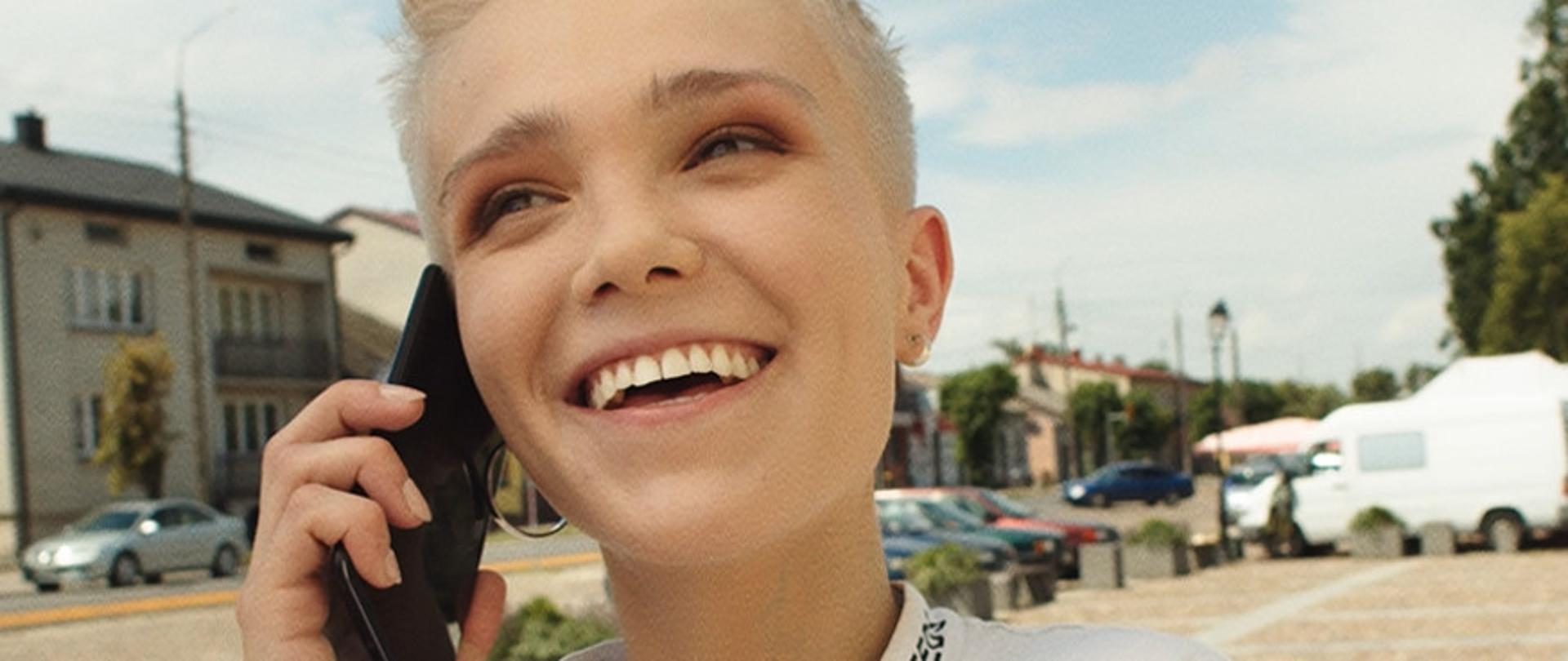 Młoda, uśmiechnięta dziewczyna rozmawiająca przez telefon