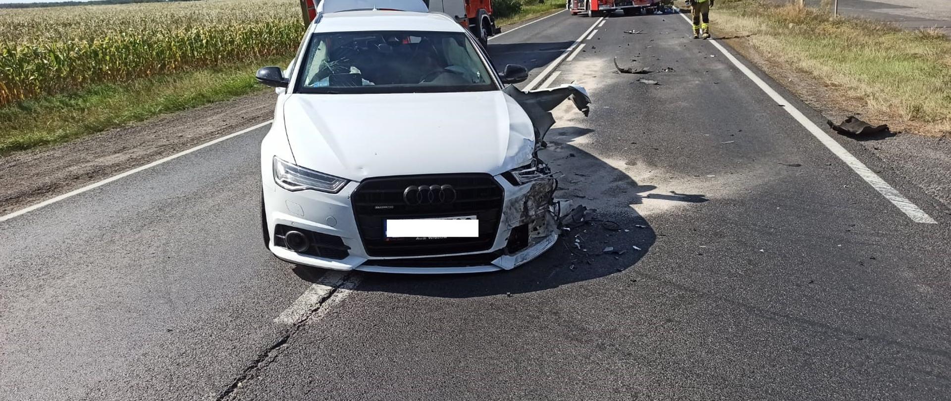 Rozbity biały samochód na drodze krajowej w tle samochody pożarnicze