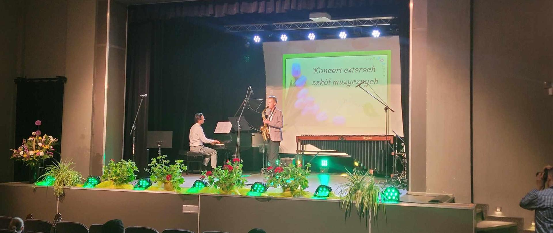 Uczeń Mieszko Grześkowiak, grający na saksofonie oraz pan Antoni Nowak przy fortepianie na scenie podczas koncertu szkół.