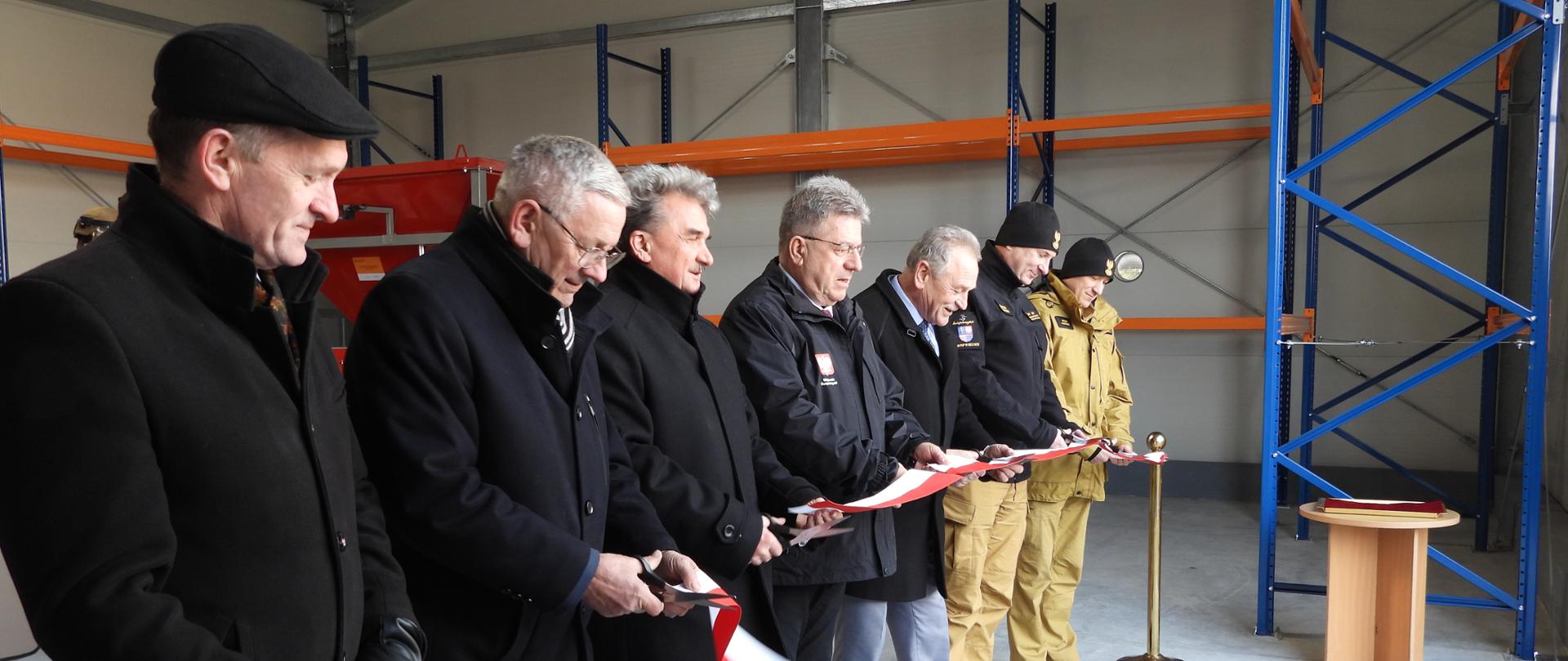 Zdjęcie przedstawia uczestników otwarcia magazynu podczas przecinania wstęgi.