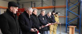 Zdjęcie przedstawia uczestników otwarcia magazynu podczas przecinania wstęgi.
