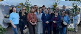 Grupa kilkunastu osób stoi i się uśmiecha do zdjęcia w tle namioty 