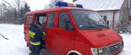 Strażacy wspierają Narodowy Program Szczepień. W centrum zdjęcia samochód strażacki, bus, czerwony. Dwóch strażaków w mundurze bojowym pomaga wsiąść do pojazdu starszej kobiecie. Samochód stoi na zaśnieżonej ulicy.