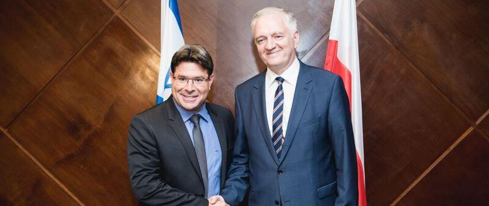 Ministrowie stoją na tle drewnianej ściany, za nimi flagi Polski i Izraela