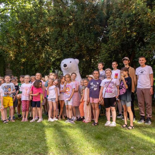 Uczestnicy pikniku rodzinnego, głównie dzieci, na wspólnej fotografii z misiem polarnym - maskotką animatorem zaproszonym na piknik.