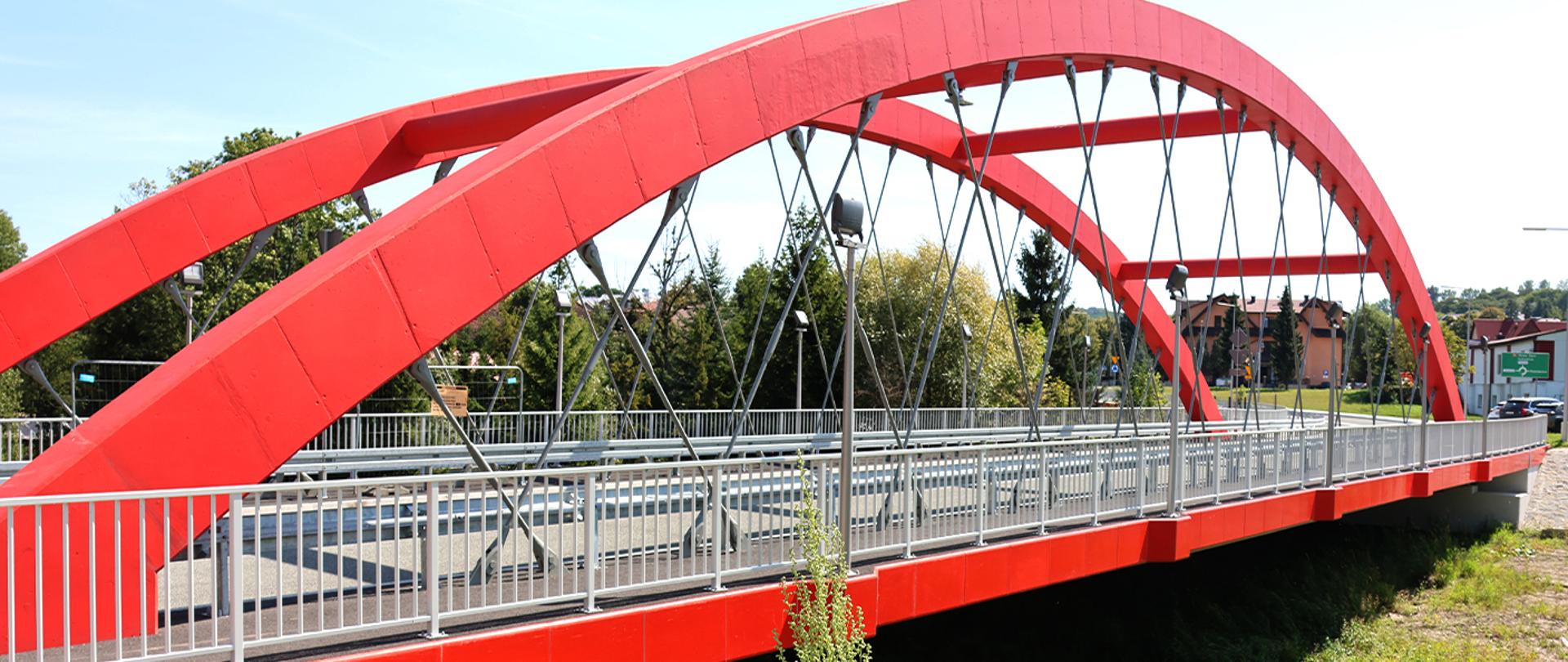Na zdjęciu widać czerwony most z drogą dla kierowców. W oddali widać domy.